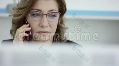 年轻的休闲女士坐在办公桌前，用笔记本电脑，<strong>接电话</strong>，打<strong>电话</strong>，微笑着在<strong>手机</strong>上说话